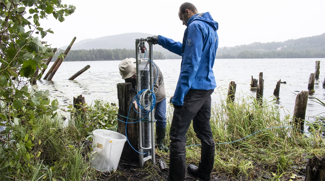 Two men stand and work with a demonstrator by water.
