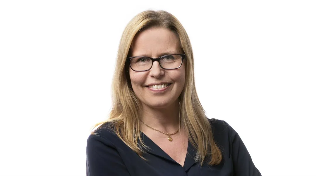 Woman with light hair, glasses and dark blouse and skirt.
