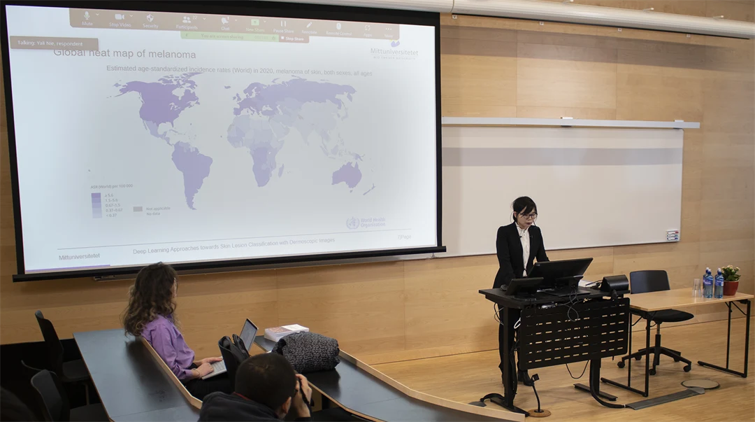 A person gives a presentation, on a large screen a picture is displayed, depicting a map of the world.