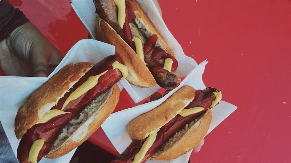 Tre händer som håller i grillade korvar.