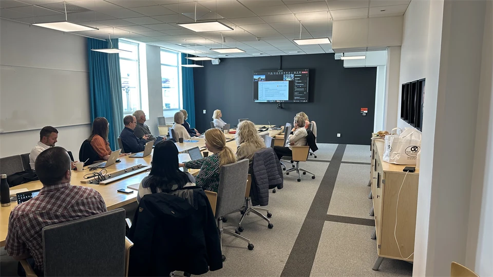 Ett konferensrum med flera deltagare runt ett bord som tittar mot en skärm