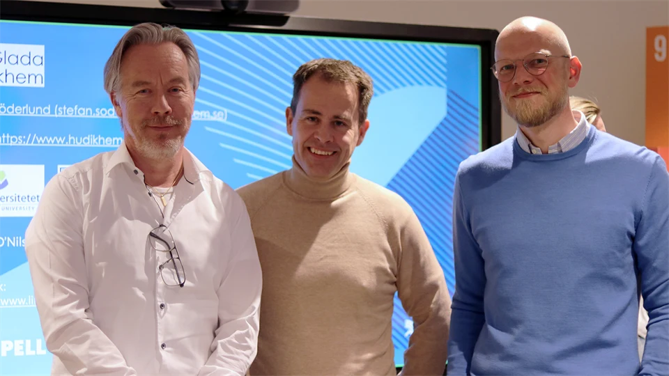 Three men stand in front of a large television screen.