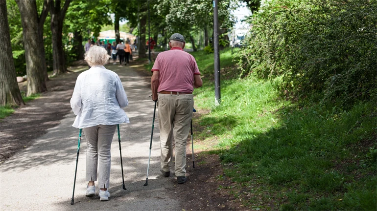 Elderly couple go Nordic walking in a park setting.