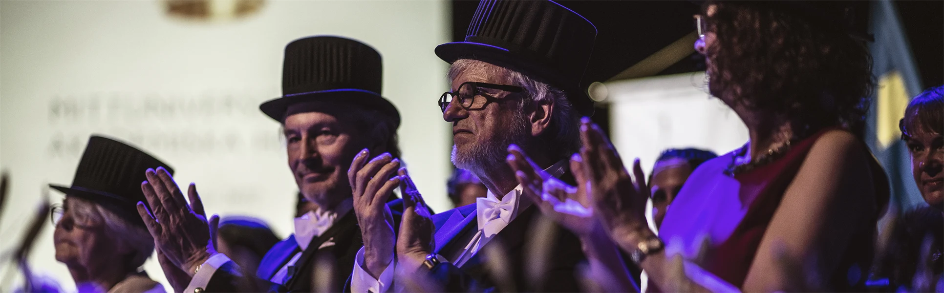 Fyra finklädda personer med doktorshattar klappar händerna. 