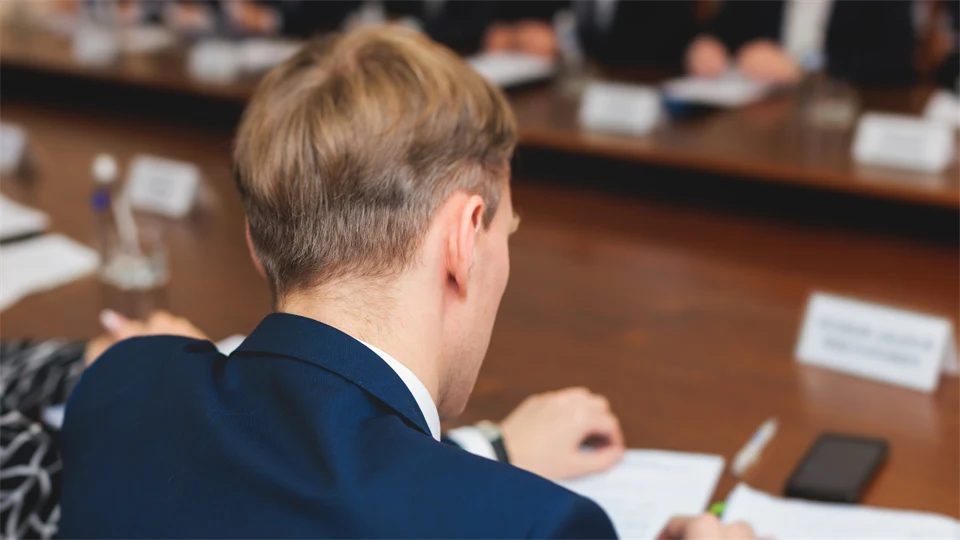 Man ser ryggen på en blond man i kavaj som sitter vid ett bord och skriver