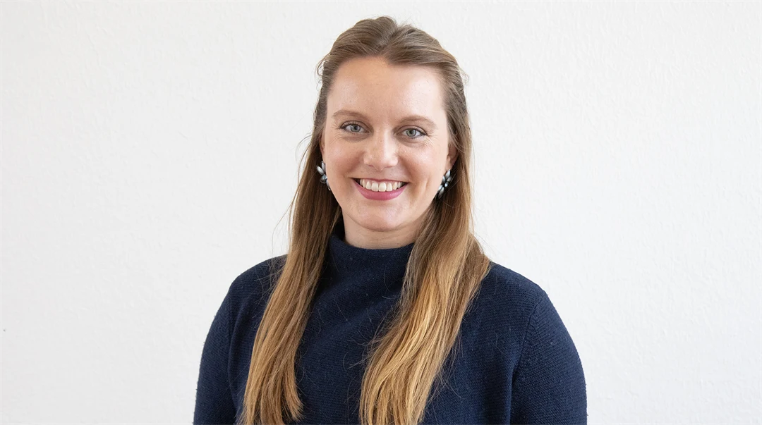 Woman with long light brown hair and dark polo shirt smiles at the camera
