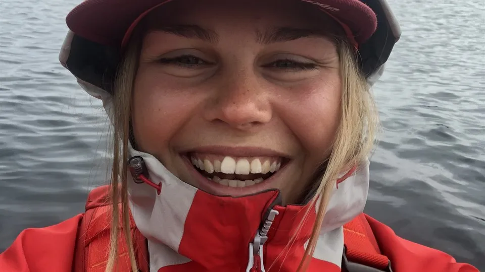 Porträtt på skrattande ung kvinna i regnställ med hav i bakgrunden.