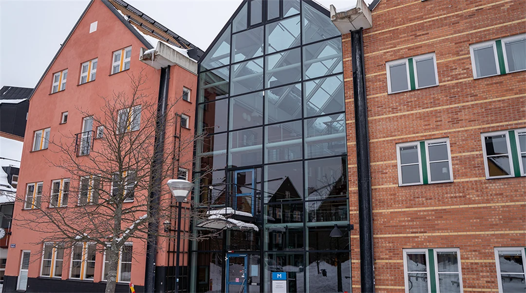 Röda byggnader ihoplänkade med en glasbyggnad.