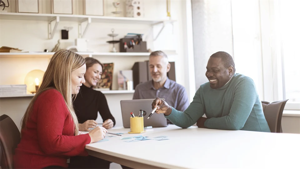 Fyra studenter runt ett bord som arbetar med en laptop och post-it lappar.
