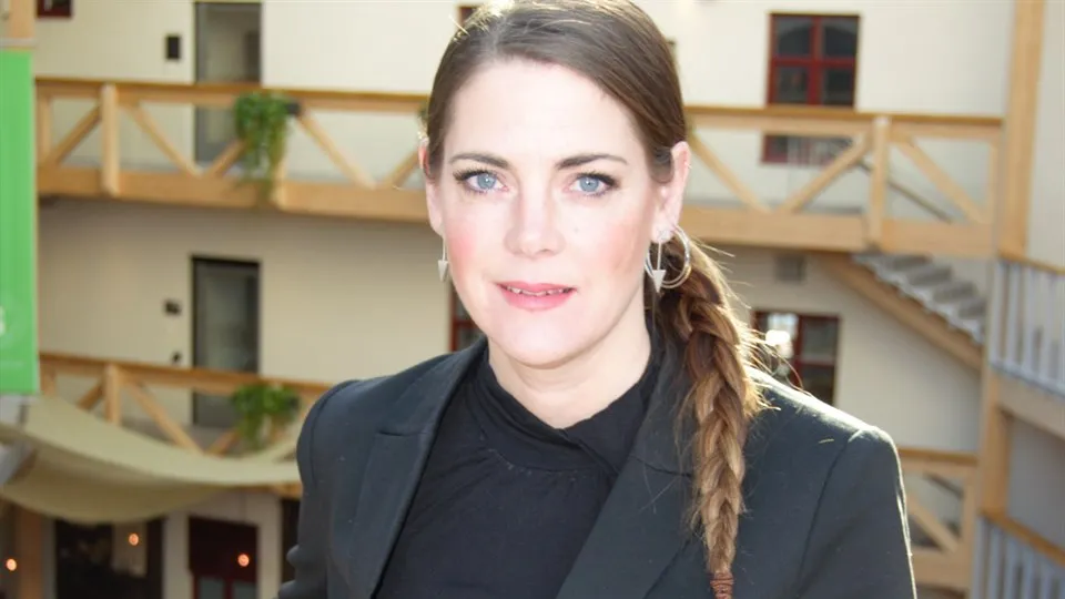 En kvinna med mörkt hår i en fläta och grå kavaj, trapphuset i bakgrunden