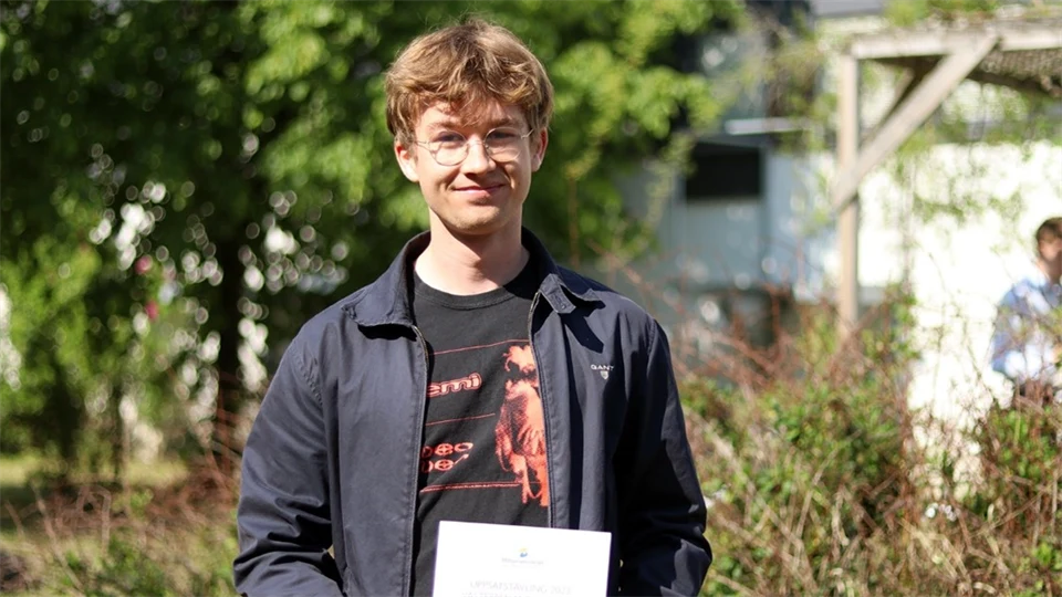 Kille ståendes utomhus och håller i sitt diplom