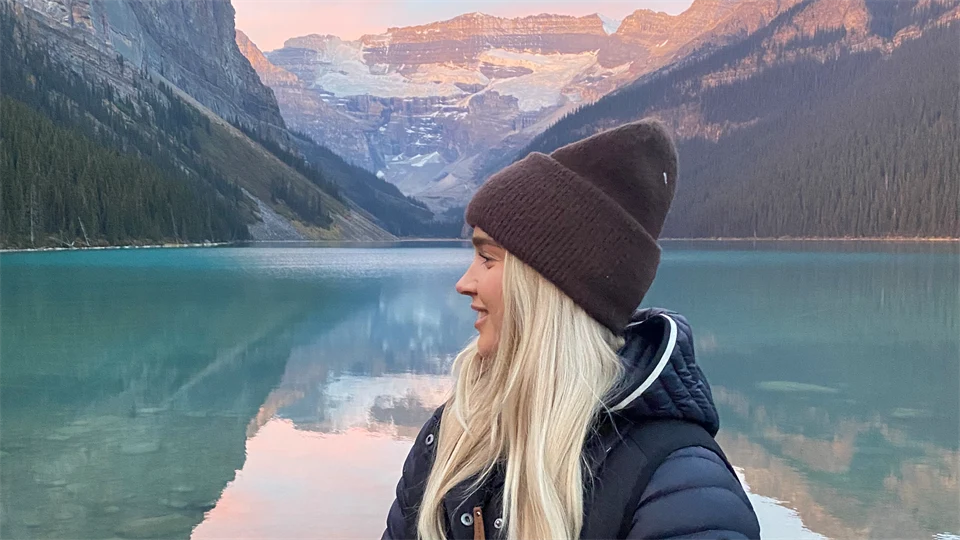 Utbytesstudenten Josefin som står vid en strand i Kanada omgiven av berg. 