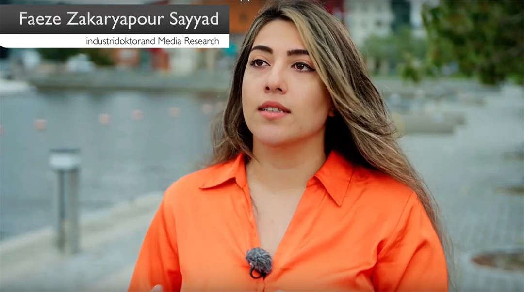 Kvinna i organge blus står vid en hamn med färgglada byggander i bakgrunden.