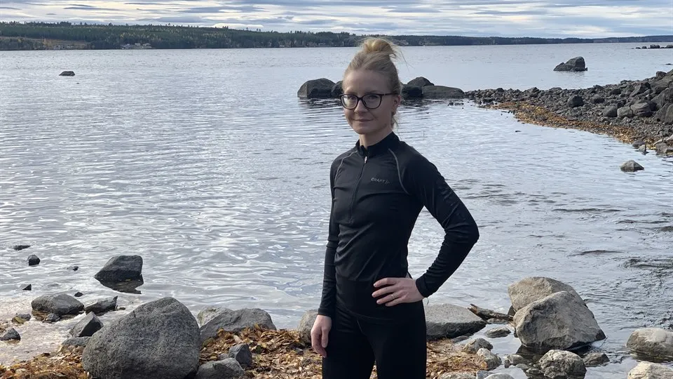 En blond kvinna i svarta träningskläder står på en stenig strand.  
