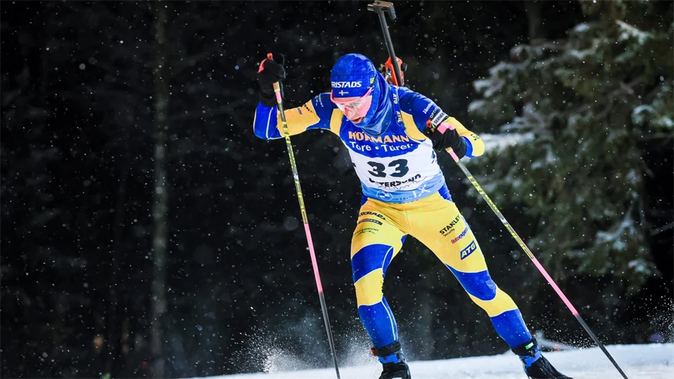 Skidskytt i svensk landslagsdress och med gevär på ryggen