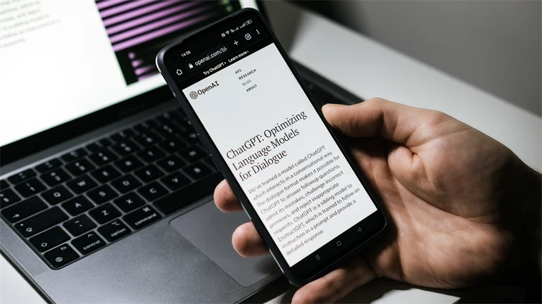 Hand holding a mobile phone with the text ChatGPT a computer in the background.