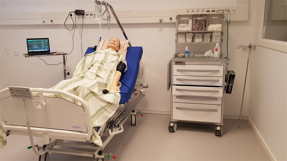 Patientsimulator i en säng i sjukhusmiljö.