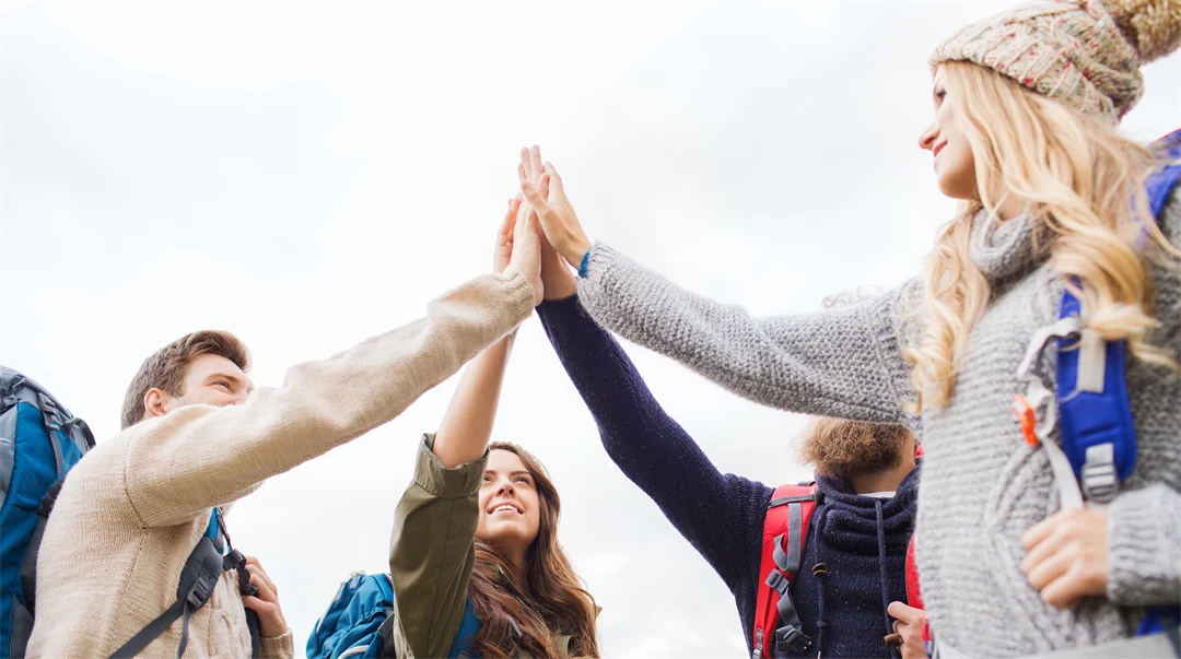 A group of people with backpacks on them stand in a ring and do a high five
