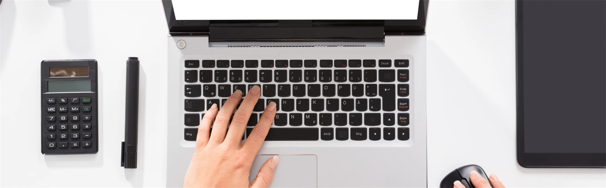 Händer knappar på en laptop, miniräknare, tuschpenna och häftmaskin ligger in till