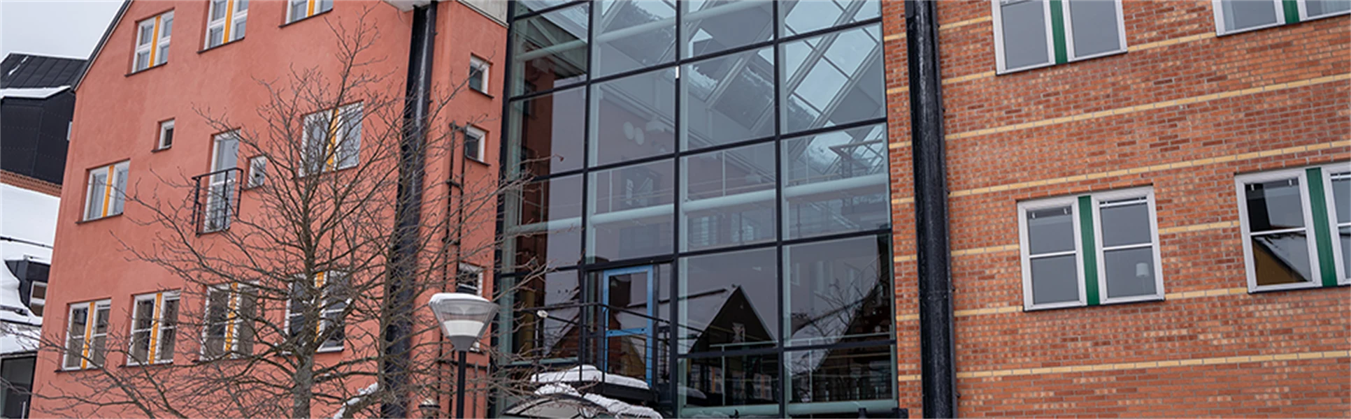 Röda byggnader ihoplänkade med en glasbyggnad.