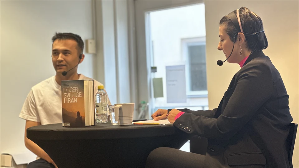 en man med vit t-shirt och svart hår samtalar med en kvinna med kort svart hår sittandes vid ett bord