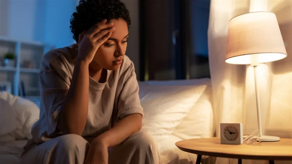 kvinna sitter på sängen och tar sig för pannan