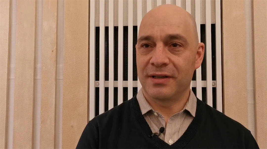 Man with shirt and black sweater being interviewed