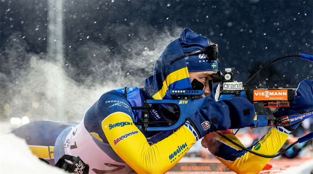 Skidskytt som ligger och siktar med sitt gevär, det ångar från ryggen.