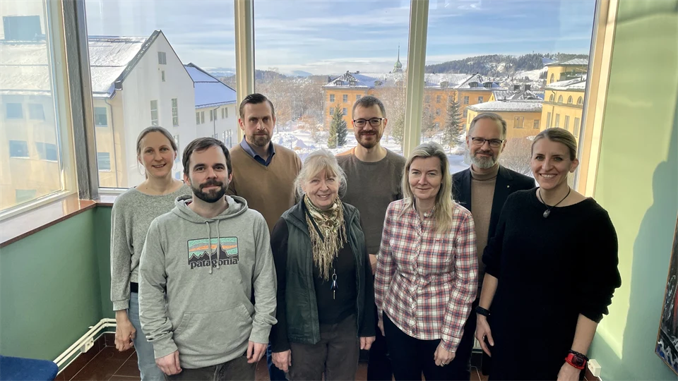 Eight people standing in front of large windows overlooking campus Östersund