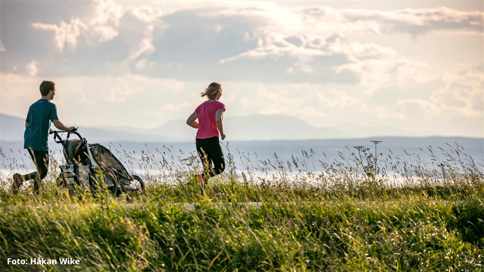 Ett par springer med en Thule-vagn längs med Storsjön