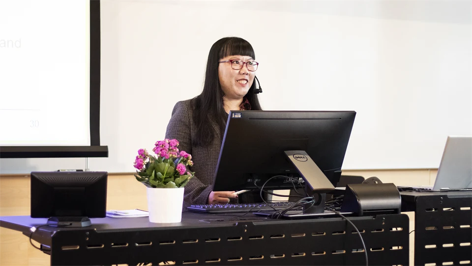 A woman stands behind a desk and presents her thesis.