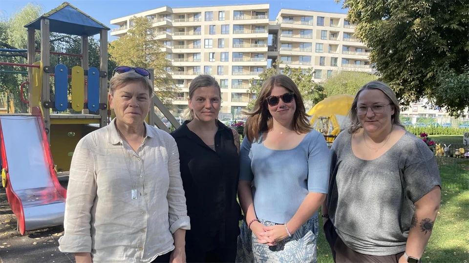 Fyra kvinnor fotograferas utomhus framför en lekpark