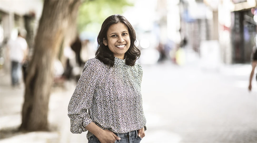 A woman in a patterned blouse and jeans smiles at the camera