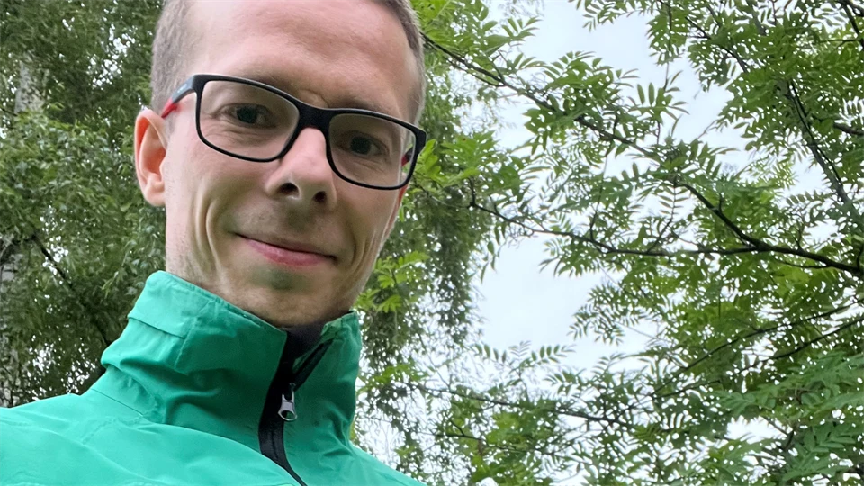 En man i grön jacka håller en liten brun hund i famnen.