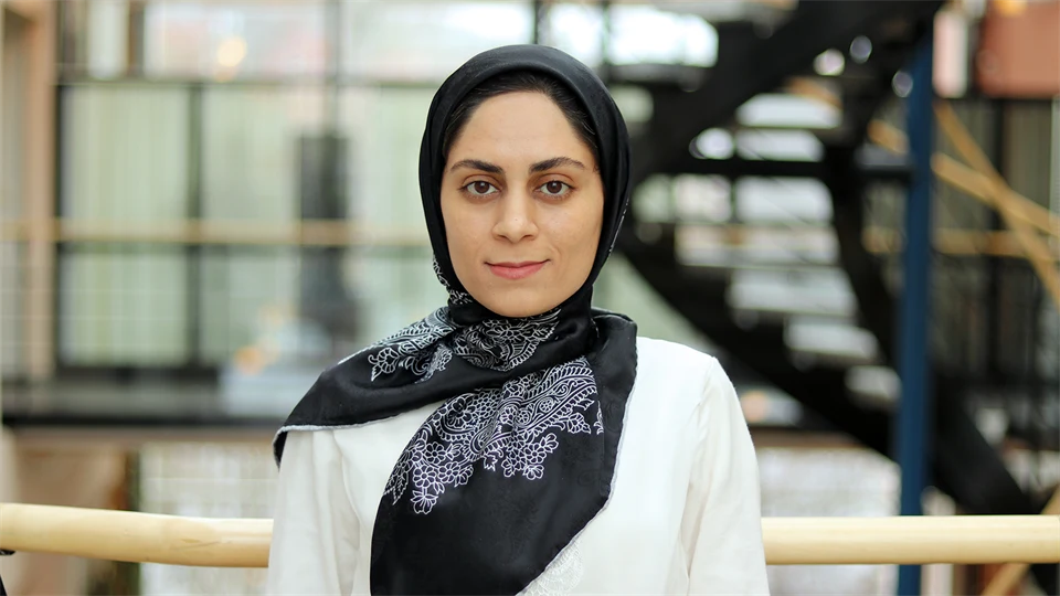 Kvinna i vit tröja med svart mönstrad huvudduk.