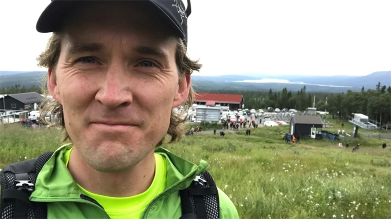 En man med keps och grön jacka med fjäll och polarull i bakgrunden 