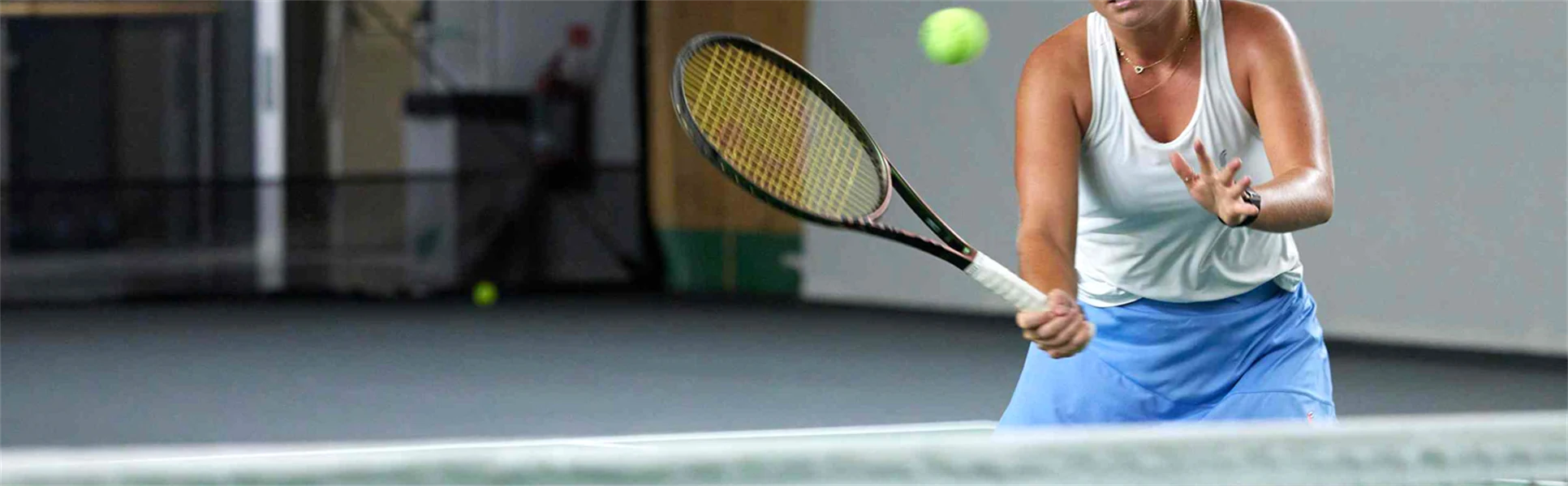 Kvinna som spelar tennis inomhus, hon står vid nät och ska till att slå en volley.