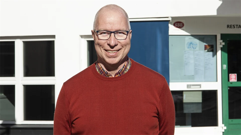 En man i glasögon och röd tröja med flera fönster i bakgrunden 