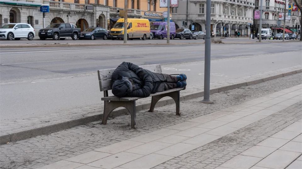 Man sover på en bänk vid trottoaren.
