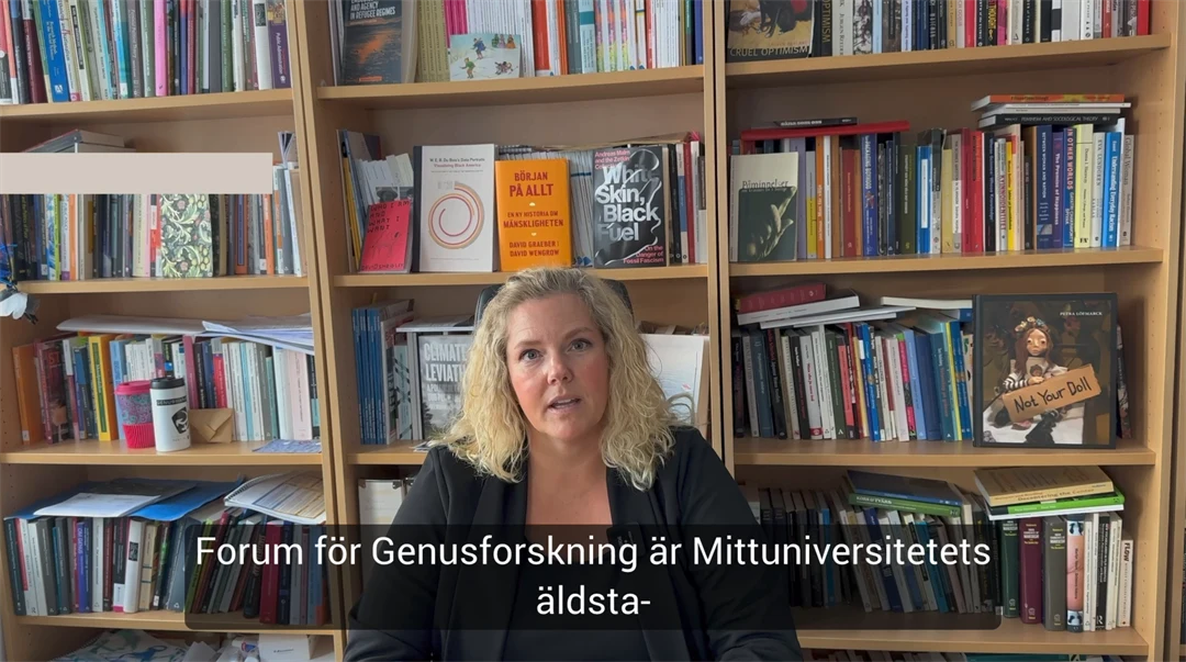 En kvinna med blont hår sitter framför en bokhylla