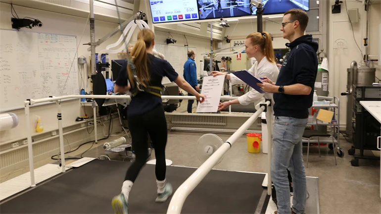 Labbmiljö med en löpare på band och forskare bredvid.