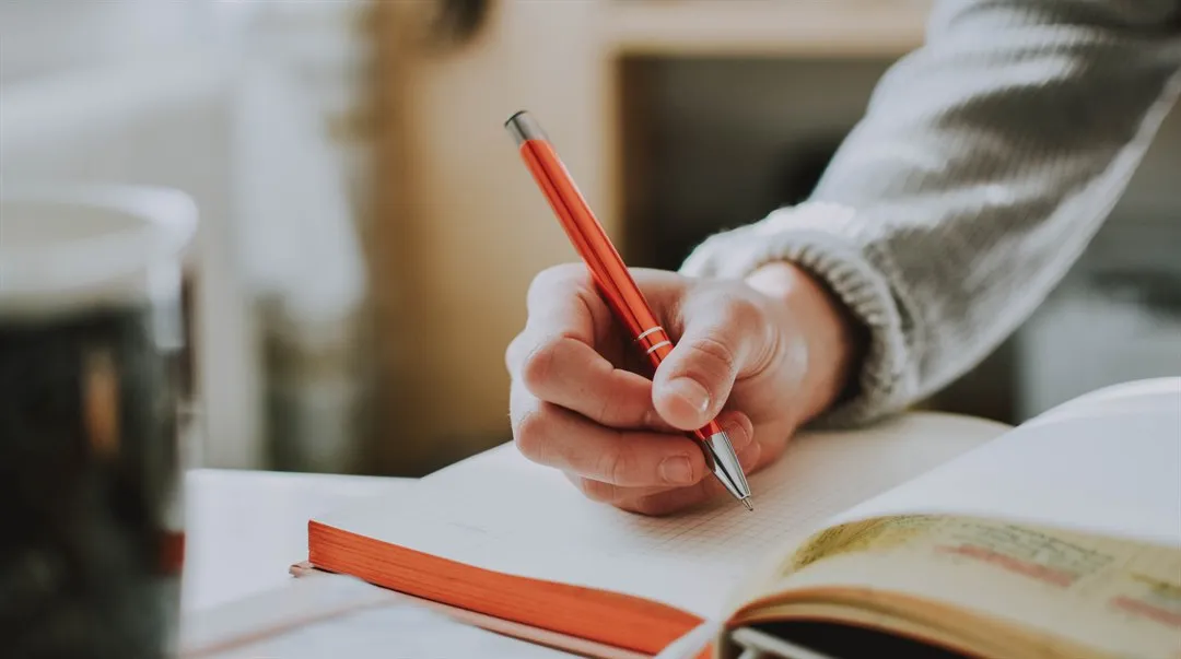 A hand holding a pen and taking notes in a notebook