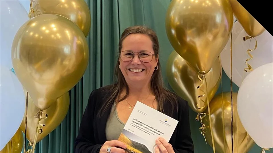 Sandra Lund står med sin avhandling framför en grön duk med ballonger på sidan om