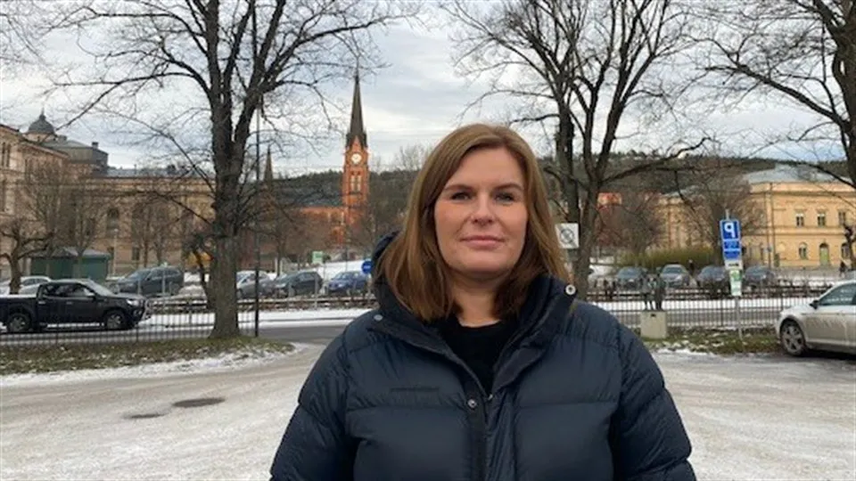 Evelina Hedström står utomhus i täckjacka. I bakgrunden syns ett kyrktorn och kala träd.