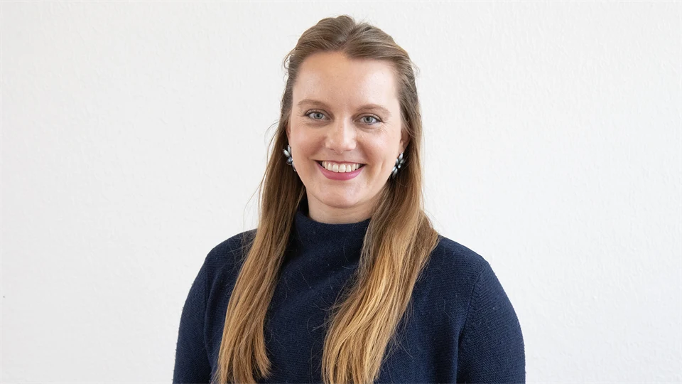 Woman with long light brown hair and dark polo shirt smiles at the camera