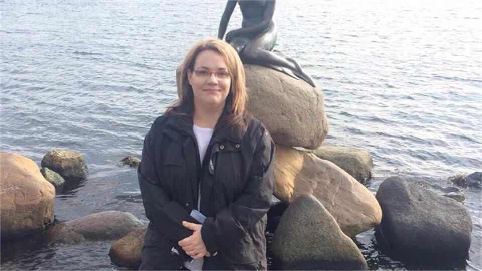 En kvinna står på en sten framför statyn "Den lilla sjöjungfrun" i Köpenhamn. 