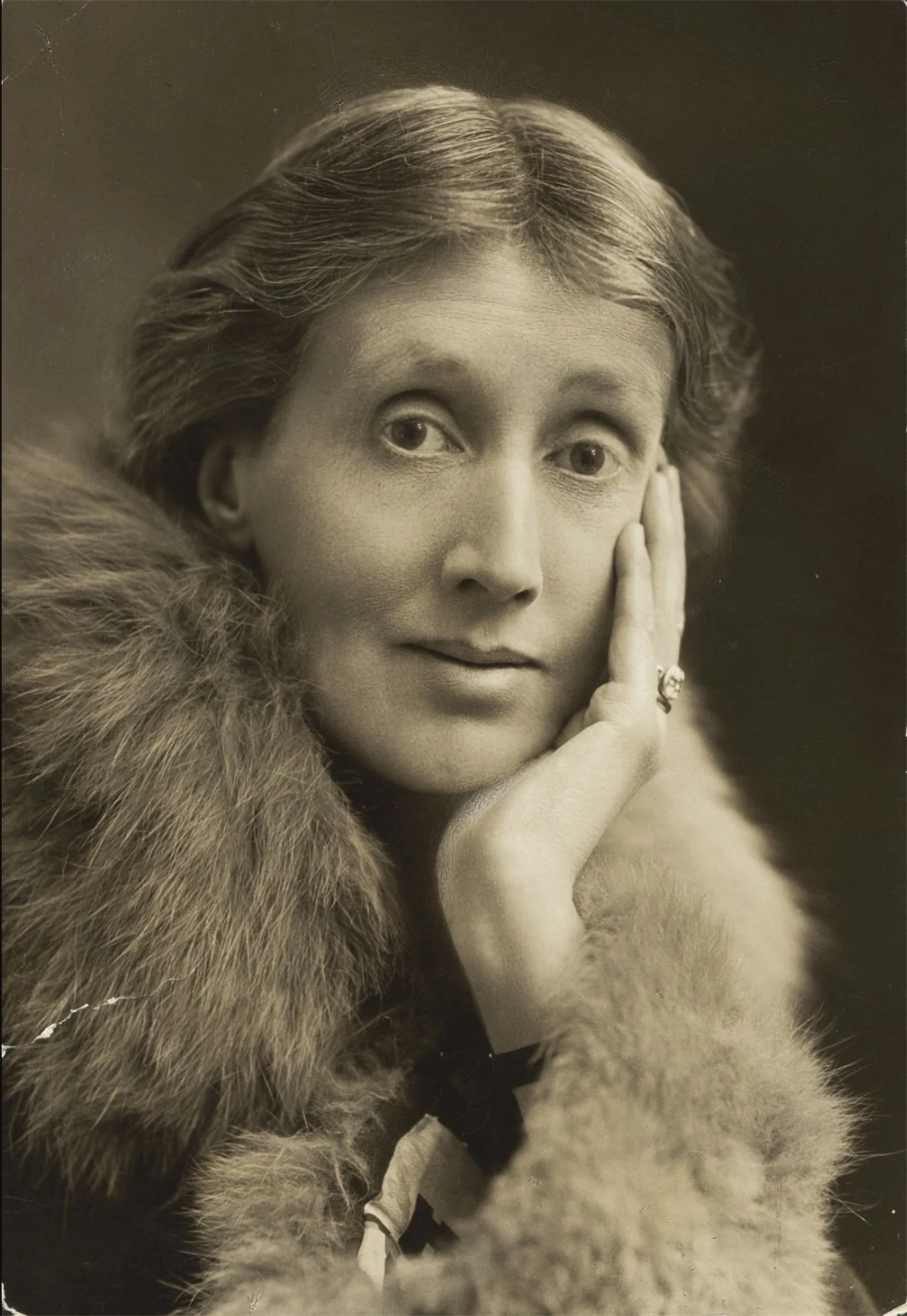 A portrait of a woman in fur who leans her head in her hand