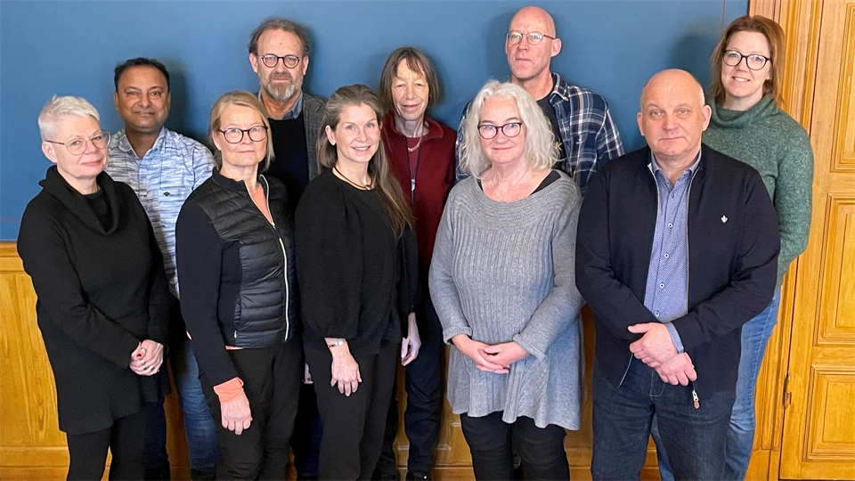 Tio personer står tillsammans med en blå vägg som bakgrund.