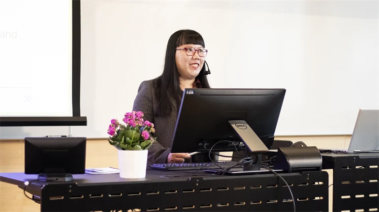 A woman stands behind a desk and presents her thesis.