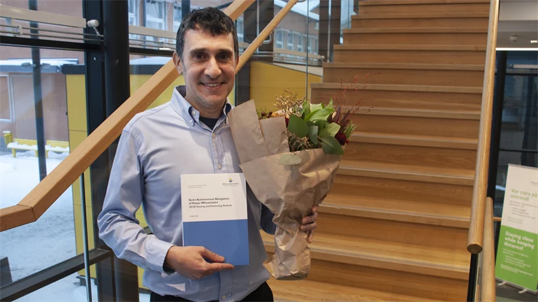 A happy man in posing infront of camera with a bouquet of flowers and his doctoral thesis.